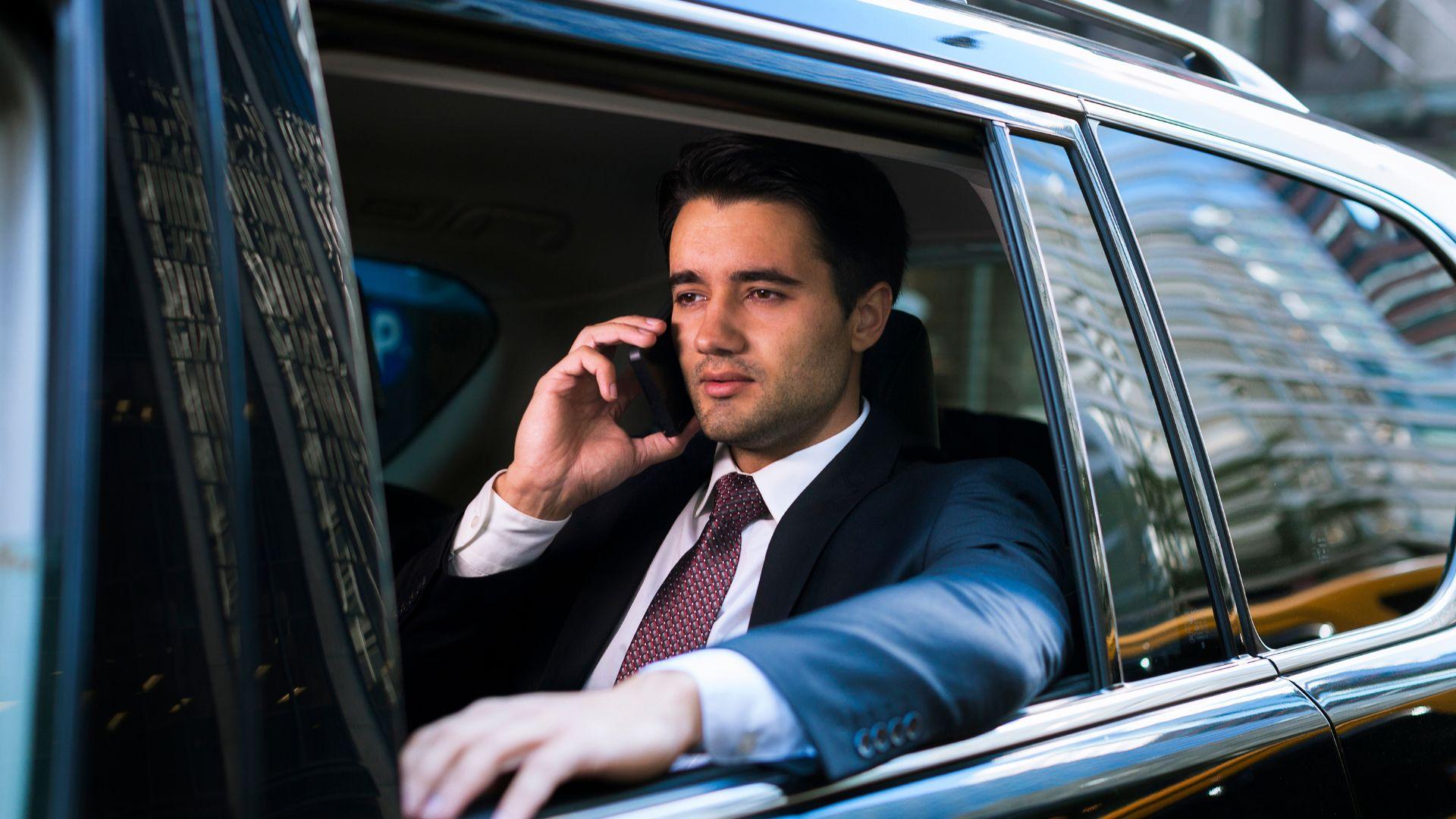 Businessman taking a phone call from the back seat of a chauffeured black car