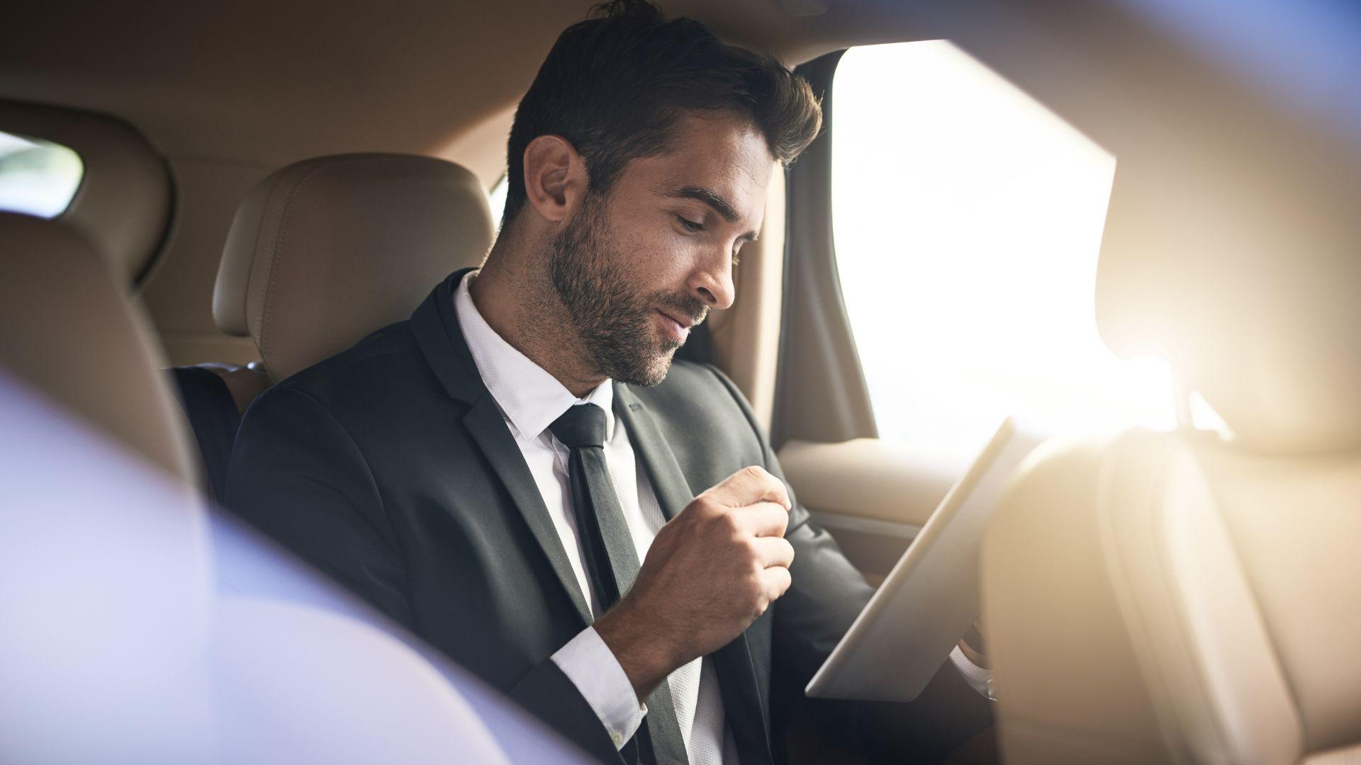 Executive reviewing documents on a tablet in the leather back seat of a chauffeured SUV